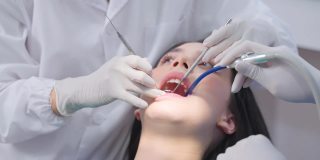 亚洲女牙医在牙科诊所用一名探险家检查年轻女孩的牙齿。牙科助理在治疗过程中协助医生使用吸痰器保持病人口腔干燥