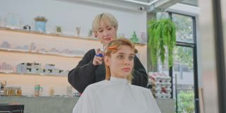 亚洲专业年轻女性发型师用剪刀为年轻漂亮的女孩客户理发。美发师交叉手臂，微笑，看着相机在美容院。