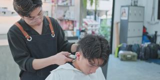亚洲专业男性发型师用剪子为年轻男性顾客理发。年轻的美发师给一个男孩换发型。美容院，时尚或理发的经营理念
