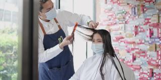 专业男性发型师在美发厅为女性顾客理发。在大流行期间戴口罩和面罩预防冠状病毒感染的男子。美容院的经营理念。