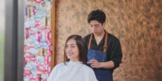亚洲专业男性发型师在美容院为年轻漂亮的女性客户理发后的发型。美发师对他的服务感到自豪，双手交叉，看着相机。