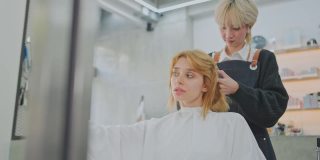 白人美女顾客用手机拍照，自拍，而亚洲专家年轻的发型师或发型师提供服务，检查她的发型在美容院或理发店理发。