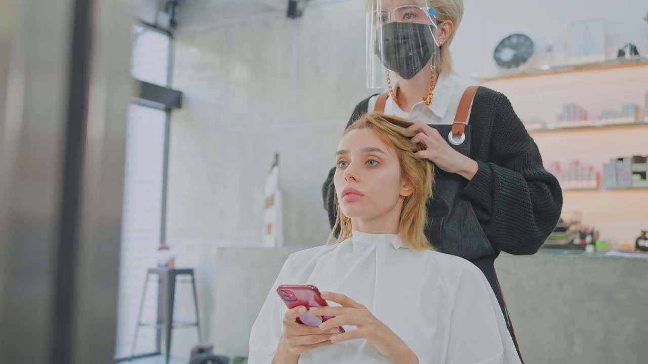 亚洲女性发型师在美容院为白人女性顾客的头发提供发型、发型和颜色建议。理发师戴口罩预防冠状病毒感染