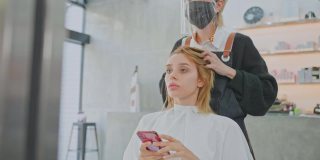 亚洲女性发型师在美容院为白人女性顾客的头发提供发型、发型和颜色建议。理发师戴口罩预防冠状病毒感染