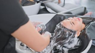 亚洲年轻女子躺在发廊洗床，在发廊由发型师洗头。漂亮的顾客一边聊天一边放松，美发师一边用水和洗发水按摩和洗头。视频素材模板下载