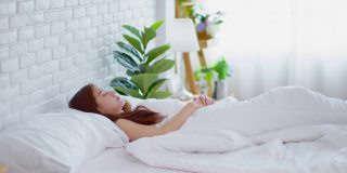 在床上醒来后，妇女伸展她的手臂，在卧室的窗户看在早上感觉如此新鲜和放松，保健概念