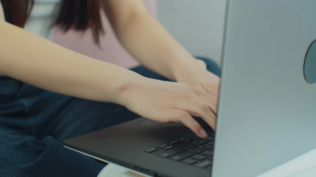 女性用手在笔记本电脑上打字，坐在家里用笔记本键盘上网。女孩在家工作在家学习电脑软件应用技术概念，近看侧面。