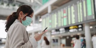亚洲妇女戴口罩以保护冠状病毒，并在机场站在飞机上检查航班