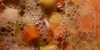 静态镜头显示极端选择性聚焦微距特写镜头的泡沫形成在一个罐装蔬菜，如甜豌豆，胡萝卜在腌汁