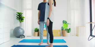 亚洲年轻情侣夫妇玩瑜伽和一起锻炼在家里的背景。锻炼身体，增加柔韧性，收紧体型。4 k慢动作。