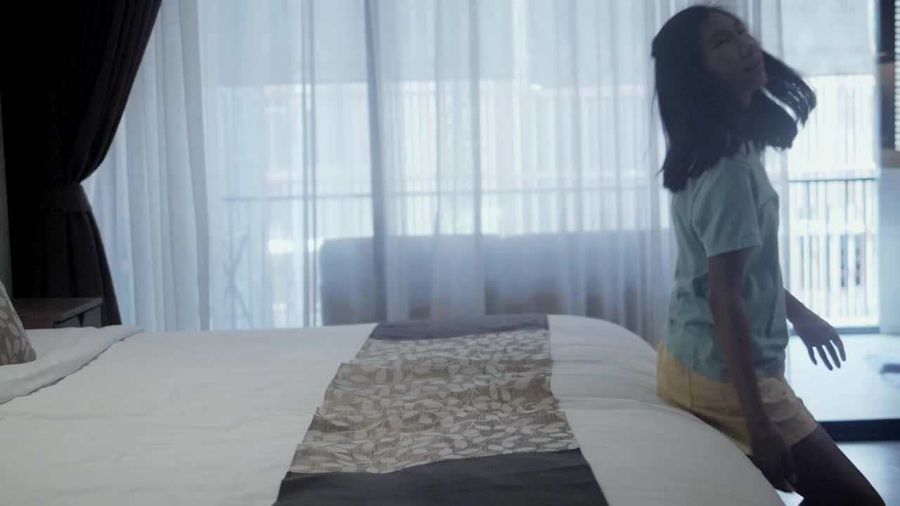 微笑的亚洲女孩躺在酒店的床上度假，生活理念。