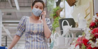 亚洲妇女戴着防护面具在购物中心买花，而在电话