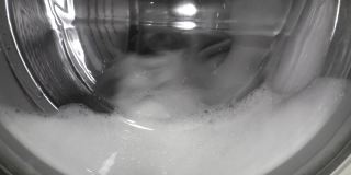洗衣机的旋转滚筒上有泡沫状的洗衣粉。在洗衣机中的洗涤过程。特写镜头。