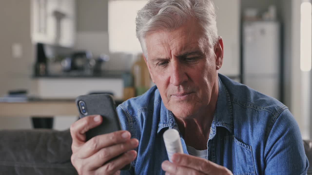 一个成年男子坐在家里的沙发上，用手机研究药物的4k视频