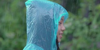 亚洲女孩穿着蓝色雨衣，喜欢下雨。孩子们在户外玩水花。缓慢的运动。