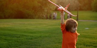 在夏日公园里，小女孩带着玩具飞机在夕阳下又跑又笑。在绿色草坪上快乐奔跑的孩子和飞机的镜头运动。