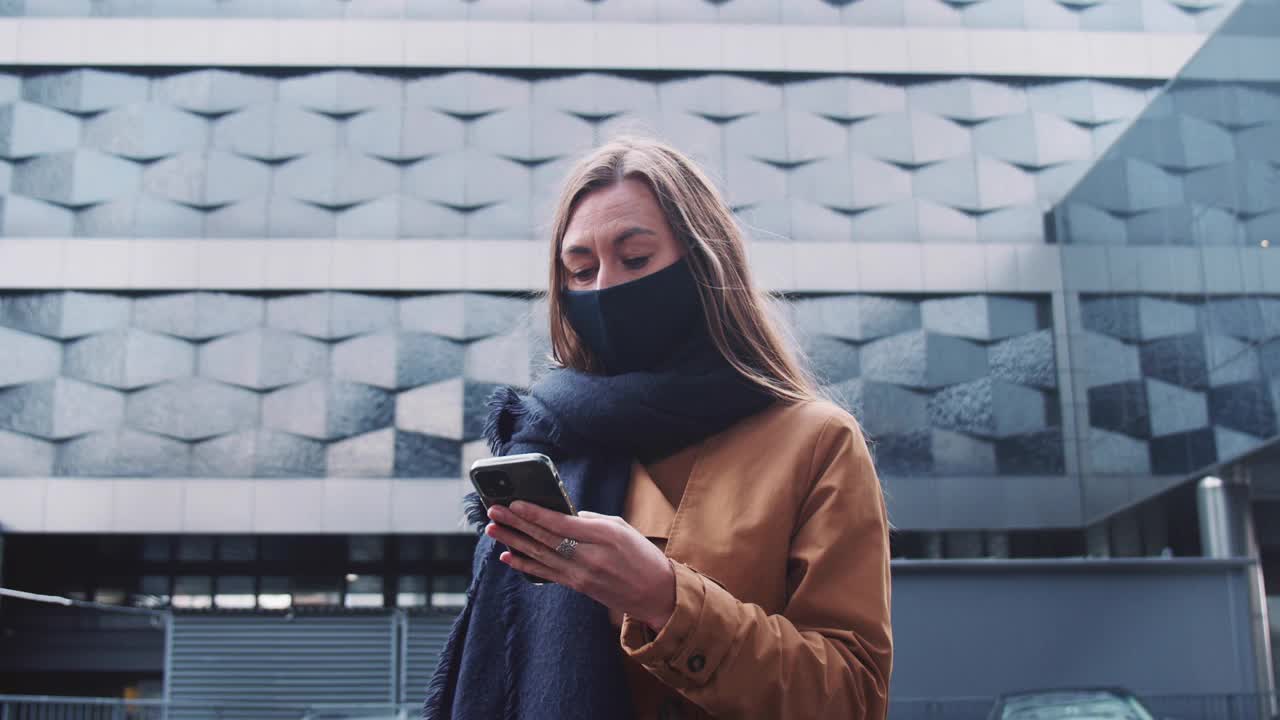 5 g网络连接。年轻美丽的商业女性戴着面具使用智能手机应用程序在一个巨大的未来主义建筑。