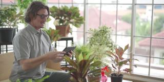 这是在新冠疫情期间快乐地在家园艺的一种爱好。一名男子正在用平板电脑给自家花园里的植物拍照