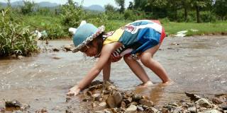 一个可爱的小女孩在一个乡村的小溪中放置一块石头作为屏障。游戏，建造水坝。童年幸福的概念。节约用水。