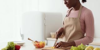 年轻的非洲裔美国母亲正在准备蔬菜沙拉，卷曲的小女儿走了过来，在厨房吃着新鲜的胡椒