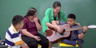 十几岁的唐氏综合症女孩在轮椅上与残疾学生团体见面练习弹吉他、跳舞、唱歌，亚洲美女老师在见面课上给予鼓励，感受快乐、积极的情绪。