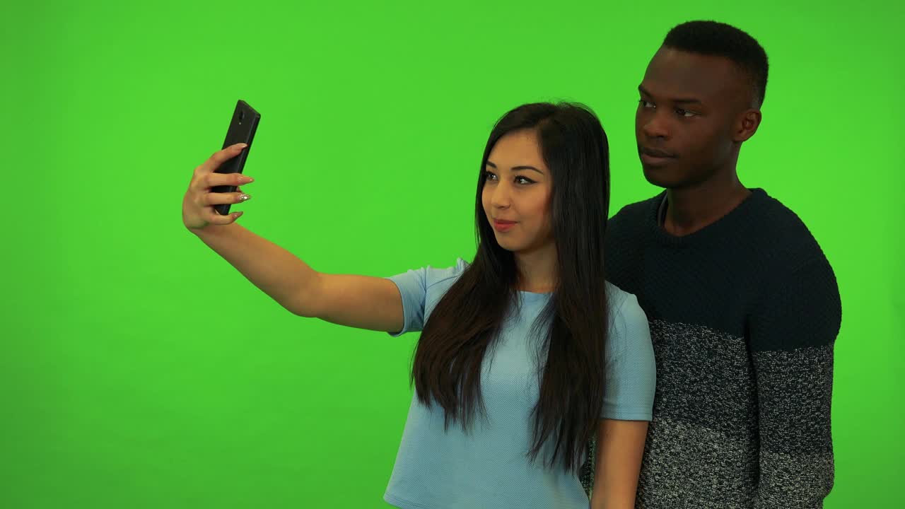 一名年轻的亚洲女子和一名年轻的黑人男子在绿幕摄影棚自拍