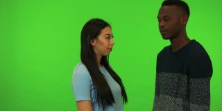 一个年轻的亚洲女人和一个年轻的黑人男人拥抱和交谈-绿色的银幕工作室