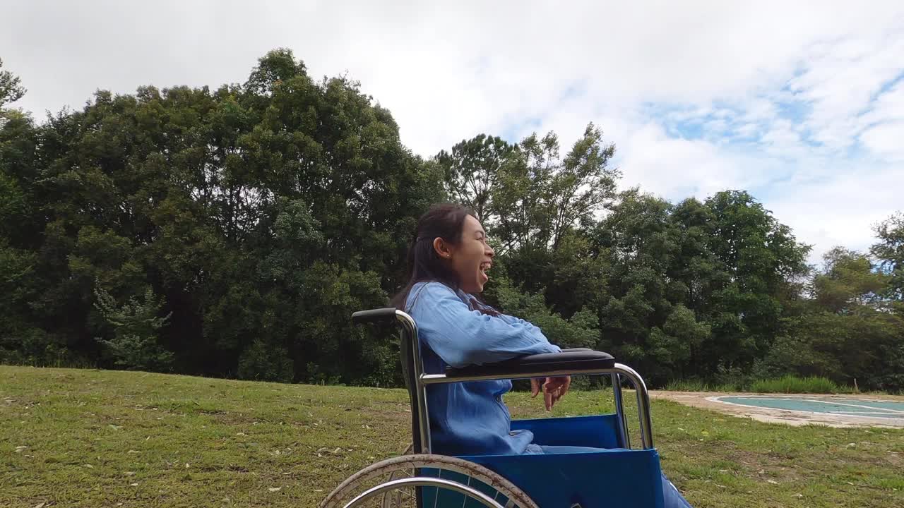 在一个阳光明媚的夏日，坐在轮椅上的快乐的残疾人妇女在春天的花园里享受大自然。