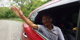 快乐的老人打开车窗，在车上看到美丽的风景，与家人享受自然之旅。祖父面带微笑，头和手伸出车窗欣赏风景。