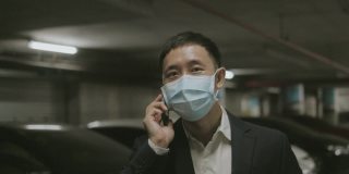 在机场航站楼办理登机手续前，带着防护口罩的亚洲中年商人与智能手机在停车场与合作伙伴讨论商业社交距离的想法——库存视频。