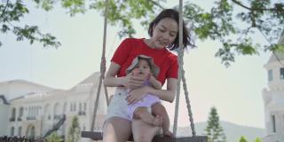 迷人的亚洲妇女母亲和可爱的婴儿在城堡白天豪华花园大树下荡秋千。女家长照顾宝宝孩子放松快乐的时间和享受阳光灿烂的日子