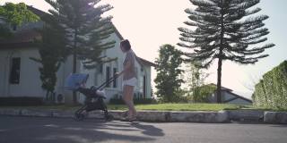 亚洲妇女母亲走在户外的婴儿在婴儿推车周围的街道村庄晚上。从家到花园，推着婴儿车散步放松。微笑快乐的家庭。