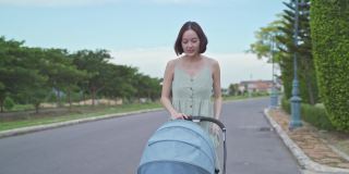 亚洲妇女母亲走在户外的婴儿在婴儿推车周围的街道村庄晚上。从家到花园，推着婴儿车散步放松。微笑快乐的家庭。