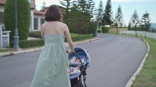 亚洲妇女母亲走在户外的婴儿在婴儿推车周围的街道村庄晚上。从家到花园，推着婴儿车散步放松。微笑快乐的家庭。视频素材模板下载