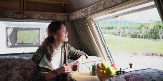 年轻的亚洲妇女喝咖啡在野营房车房车在自然