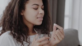 开朗的年轻非洲裔美国妇女吃药和在客厅内部的一杯水视频素材模板下载
