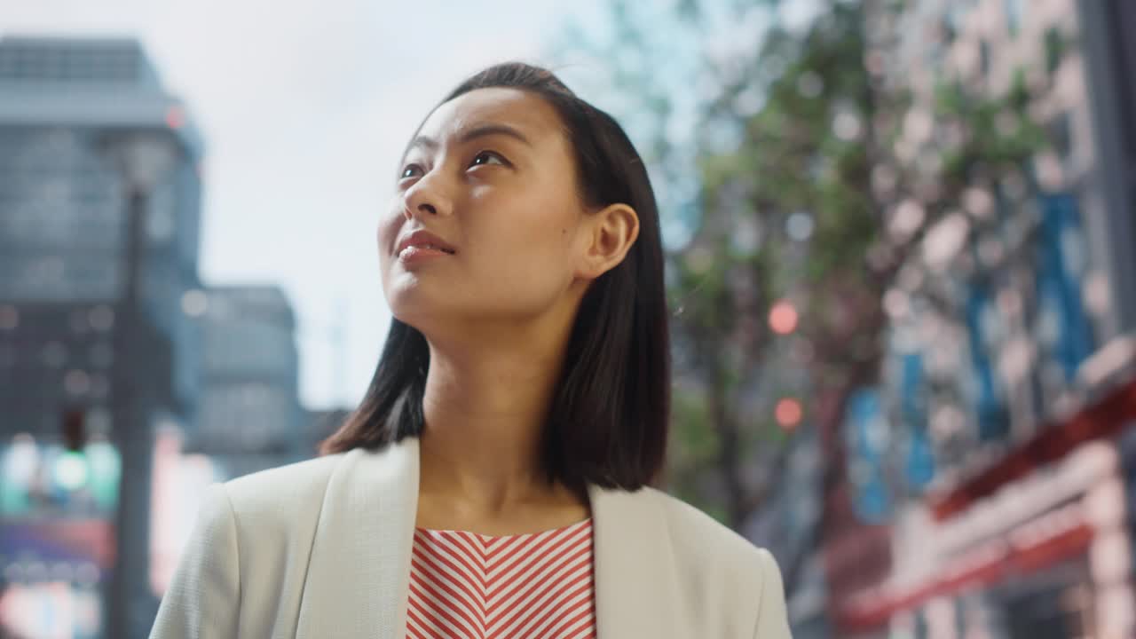 美丽的日本女性的肖像穿着漂亮的休闲衣服在街上摆姿势。在大城市生活的成功女性。背景与办公楼和广告牌。