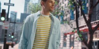 一个快乐英俊的年轻人的肖像，穿着休闲的衣服走在街上。都市时尚男模的都市生活方式。背景与办公楼和广告牌。
