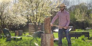 阳光明媚的春日里，一个戴着草帽穿着格子衬衫的男人正在花园里劈柴