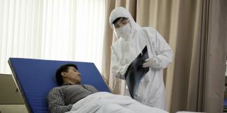 医生佩戴个人防护装备预防COVID-19。医生在病房向病人描述肺部x光片。质量差的治疗