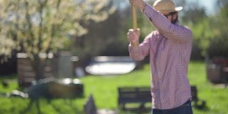 阳光明媚的春日里，一个戴着草帽穿着格子衬衫的男人正在花园里劈柴