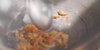 在炉子上的炒锅里用油煸炒新鲜的红辣椒，用勺子把炒熟的蔬菜放在炒锅里