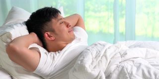 一个年轻的亚洲人躺在床上望着窗外。