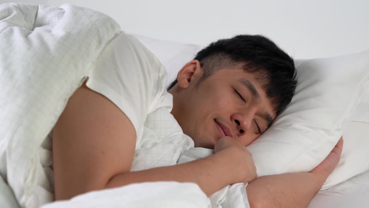 快乐的亚洲年轻人早上睡在舒适的床上。