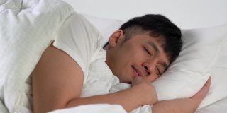 快乐的亚洲年轻人早上睡在舒适的床上。