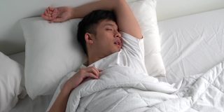 年轻的亚洲男人在床上睡觉时打鼾。