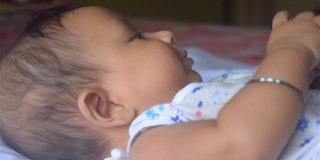 可爱的小男婴在床上玩手。一个月大的可爱的婴儿蹒跚学步的婴儿特写脸部肖像。印度的种族。前视图。儿童保健背景。资料片。
