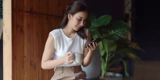 放松的女人用咖啡和智能手机度过早上的时间。