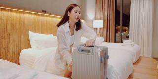 美丽的女人在舒适的酒店房间的床上打开行李箱。