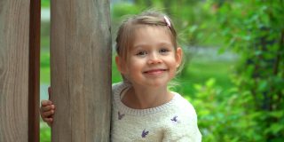 在绿色的夏日公园里，小女孩看着相机，笑了起来。快乐的孩子在户外玩耍。孩子在操场上的院子里